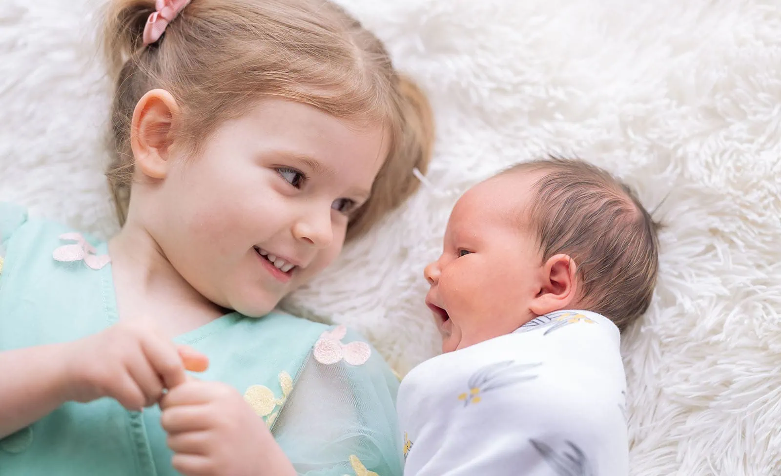 baby joshua's newborn photo shoot 30 Siblings bonding on a soft fluffy rug.