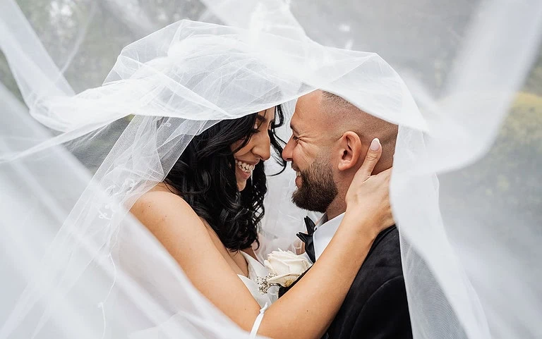 Bride and groom embrace under veil on wedding day, expressing love and happiness.