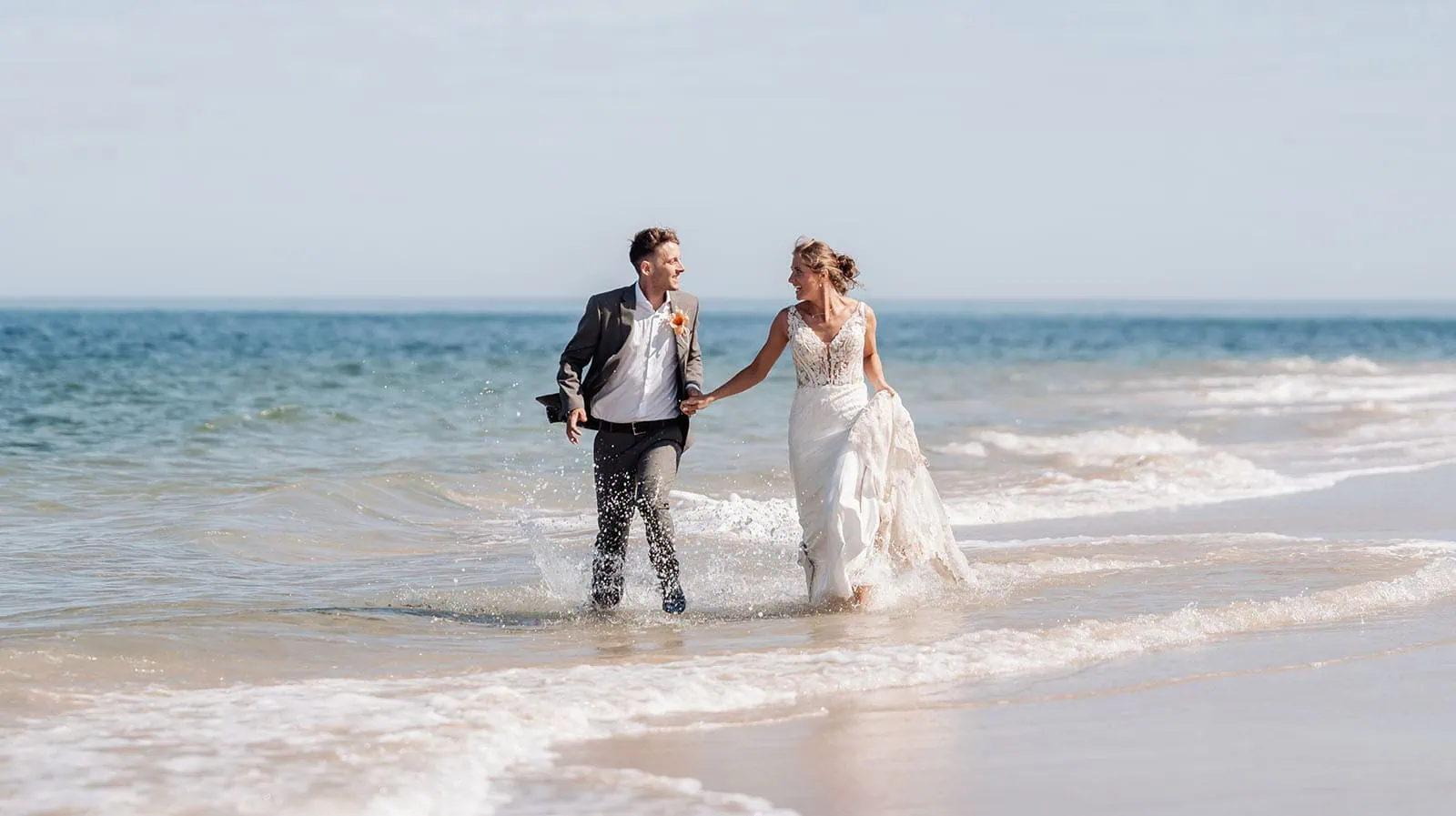pt noarlunga underwater wreck the dress shoot - jess & jack 4 Wedding couple running joyfully on sunny beach, ocean waves splashing around, expressing love and happiness.