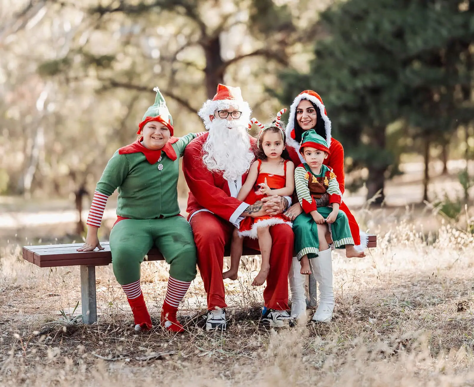 last minute father christmas photoshoot 38 Festive family in Christmas costumes sitting on park bench outdoors with Santa.
