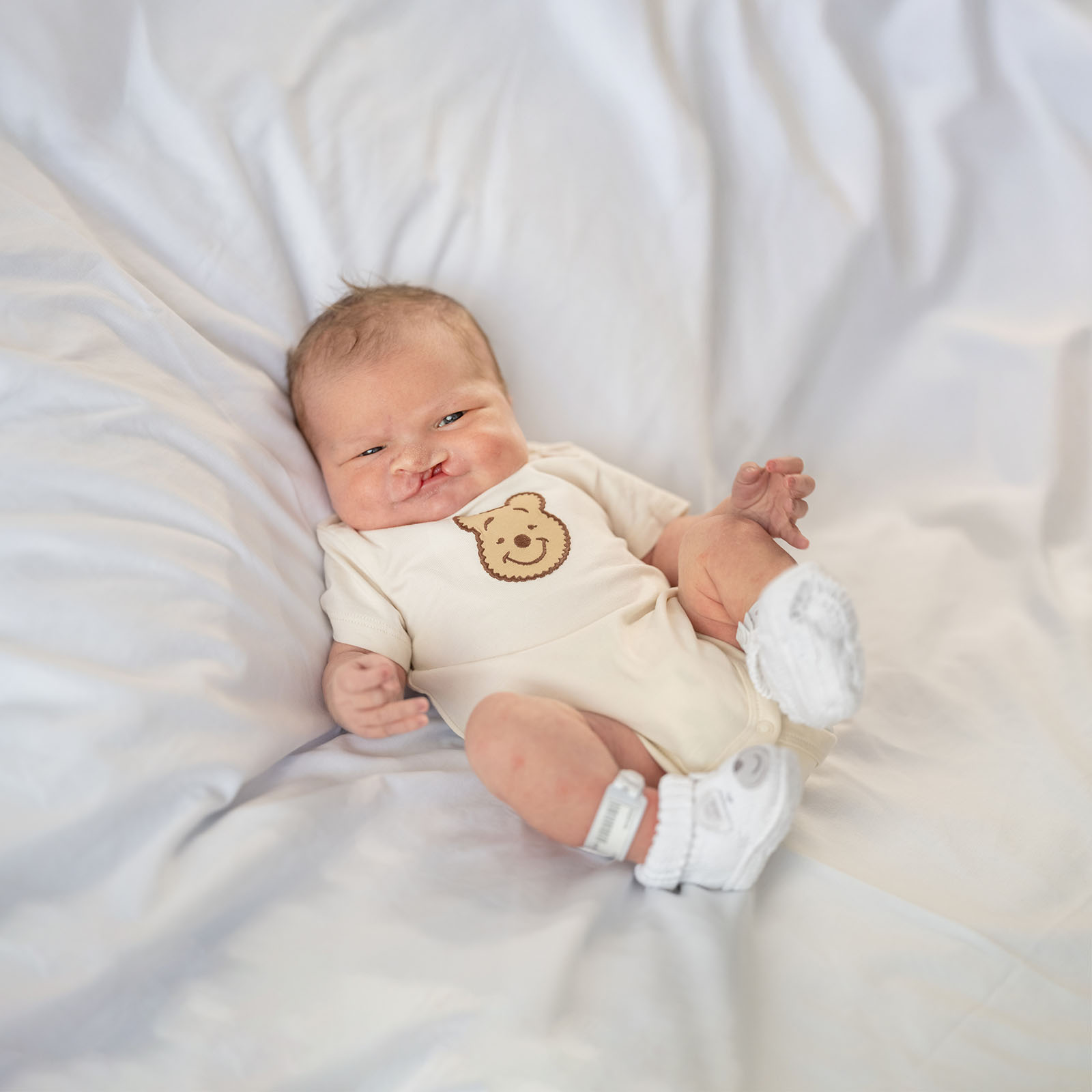 baby walker - flinders medical center newborn photography 6 Newborn baby resting peacefully in cream onesie with bear graphic on white blanket.