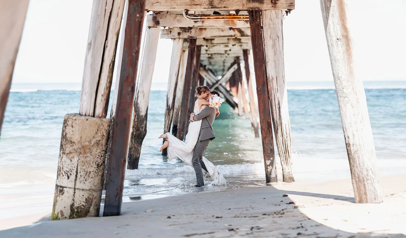 pt noarlunga underwater wreck the dress shoot - jess & jack 1 Romantic couple under rustic pier celebrating wedding with love, joy, and vibrant flowers.