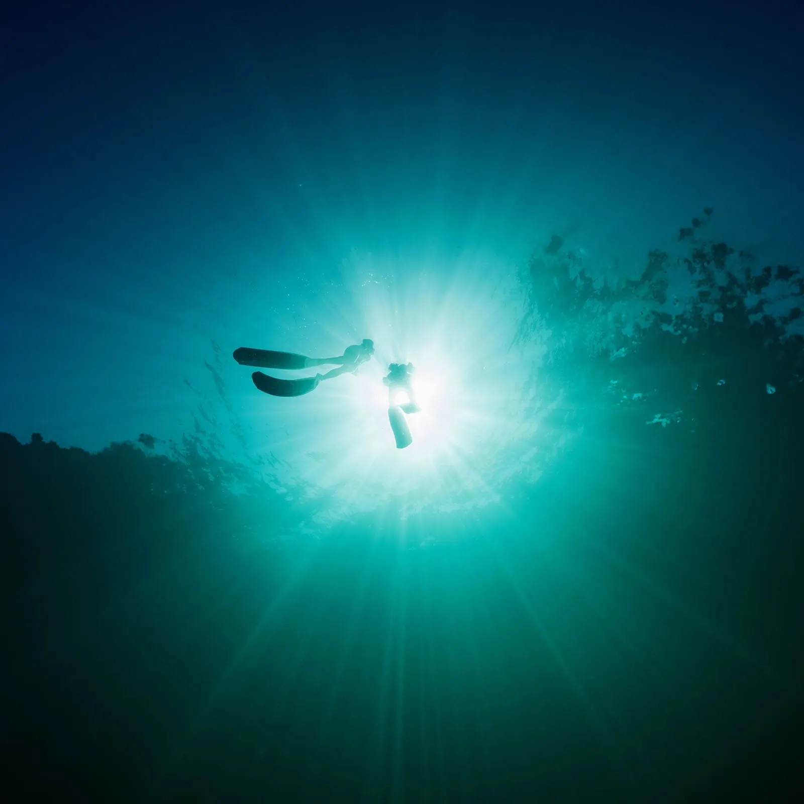 pt noarlunga underwater wreck the dress shoot - jess & jack 10 Silhouetted diver amidst sunbeams in tranquil turquoise underwater scene.