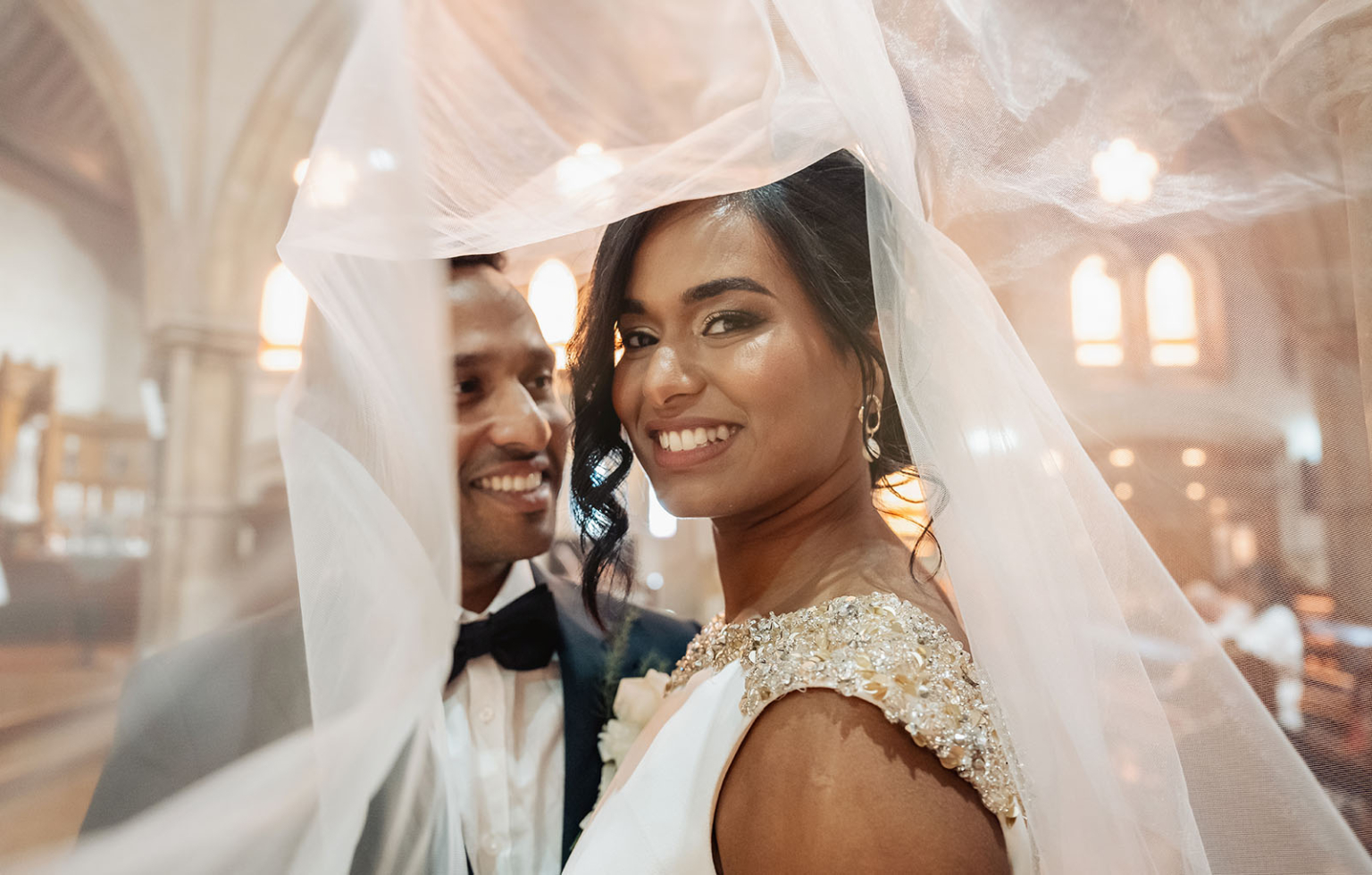 the many benefits of hiring professional wedding photographers 4 Newlywed couple smiling under veil in elegant church setting.