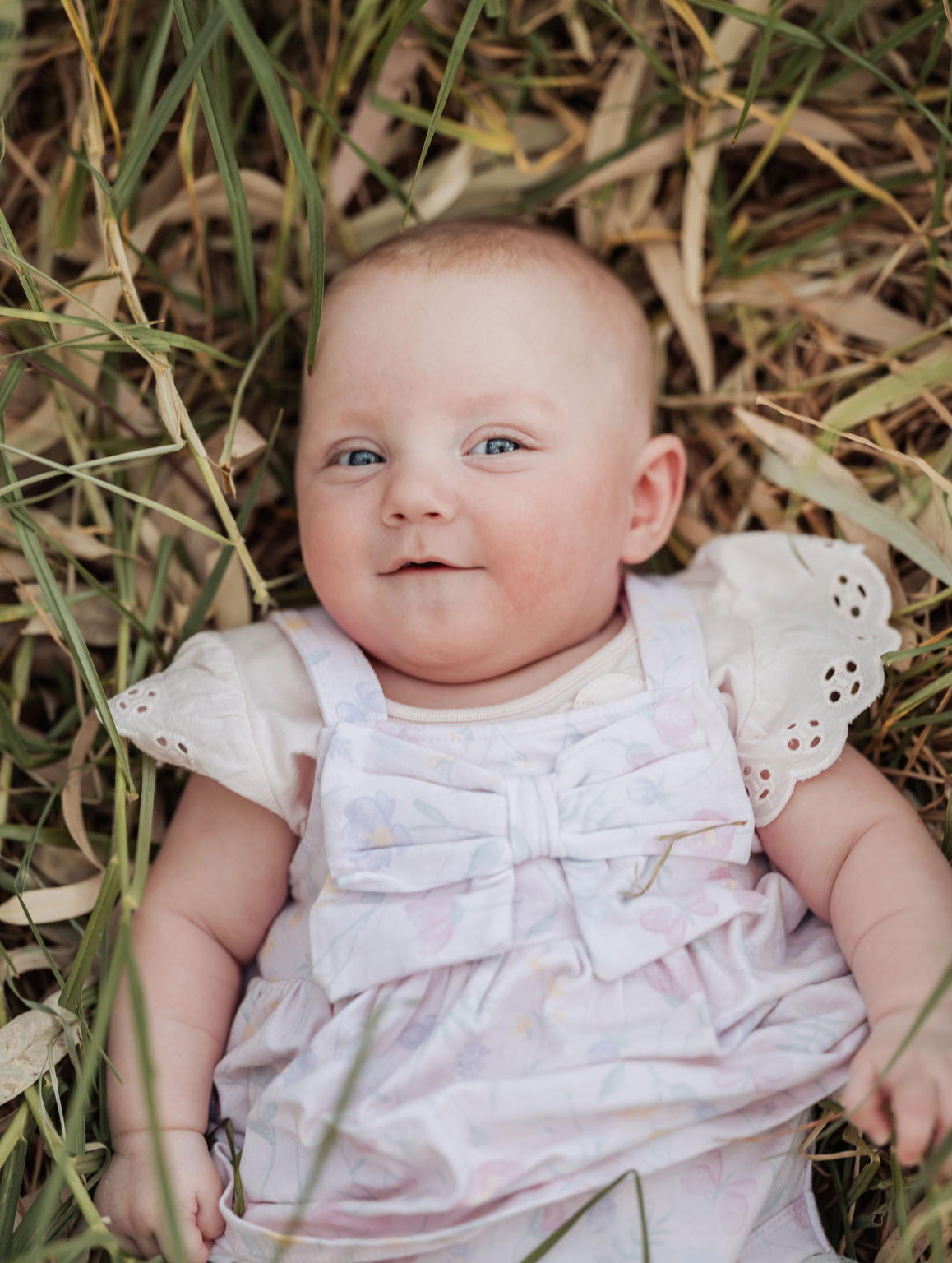 carisbrooke park family photoshoot 75 Baby lying on grass in pastel dress, blue eyes gazing upward, serene and tranquil expression.