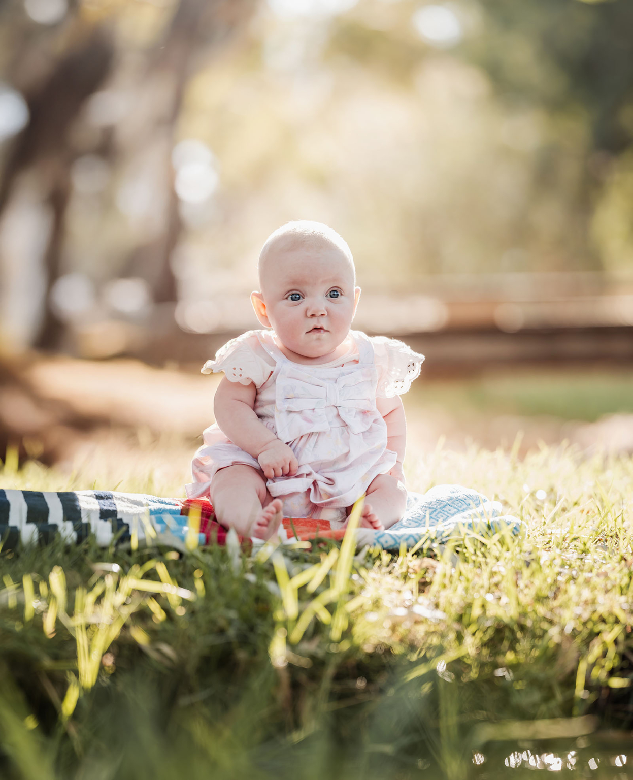 carisbrooke park family photoshoot 67 Adorable baby in pastel outfit on blanket in sunny park setting.