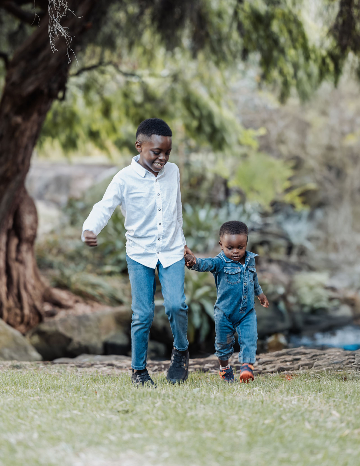 family photoshoot in veale gardens 11 Children walking hand-in-hand on green grass, under a tree, enjoying playful outdoor moments.