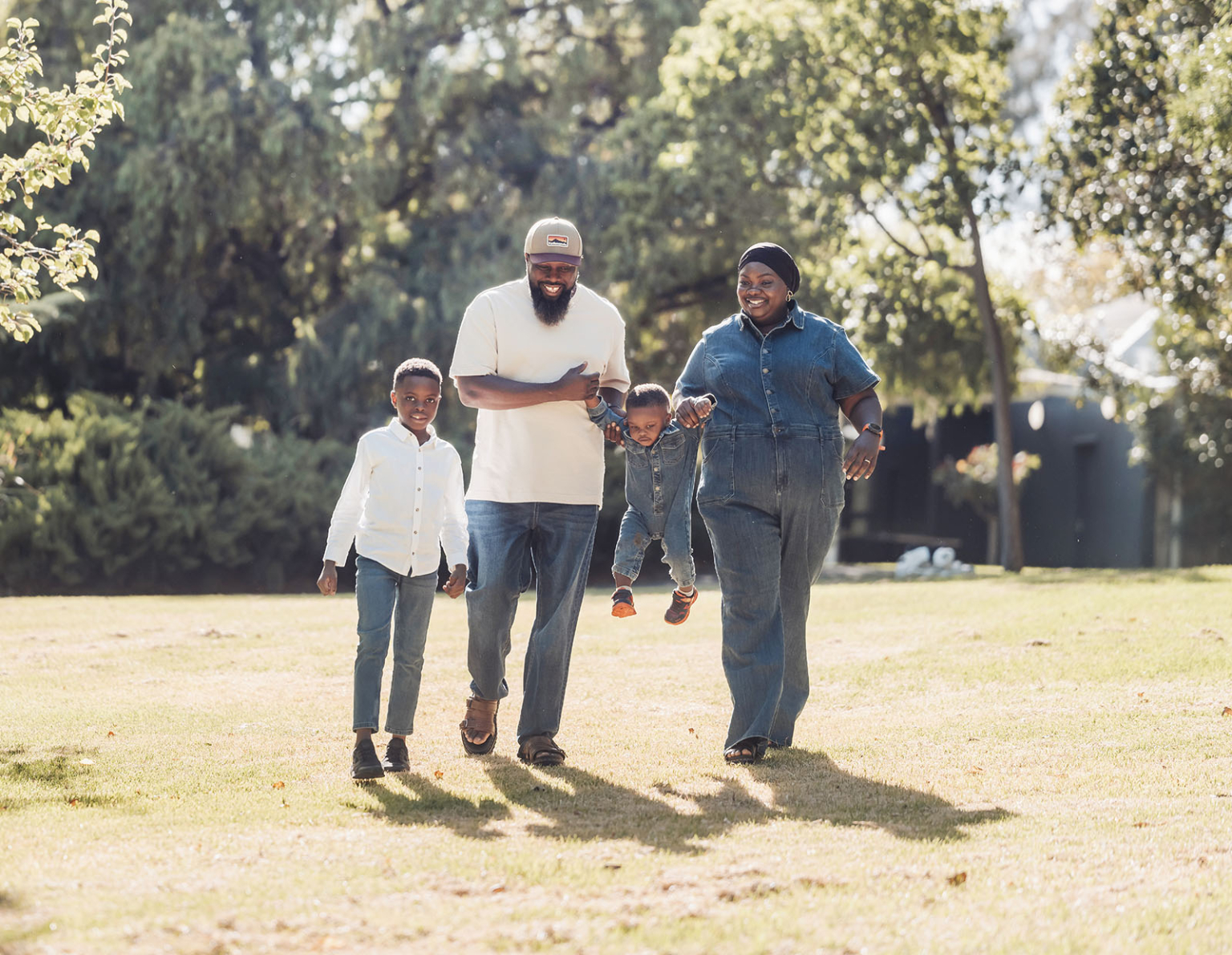 family photoshoot in veale gardens 8 Happy family enjoying a sunny day at the park, surrounded by greenery and trees.
