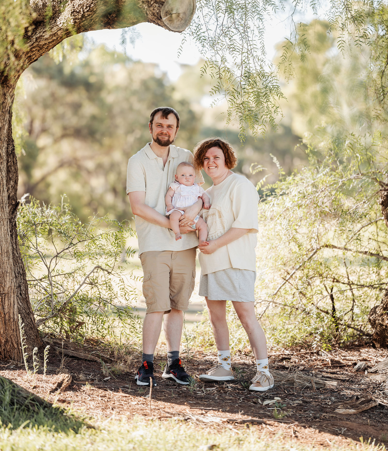 carisbrooke park family photoshoot 61 Happy family under tree in nature, enjoying sunlight with baby, capturing joyful outdoor moment.