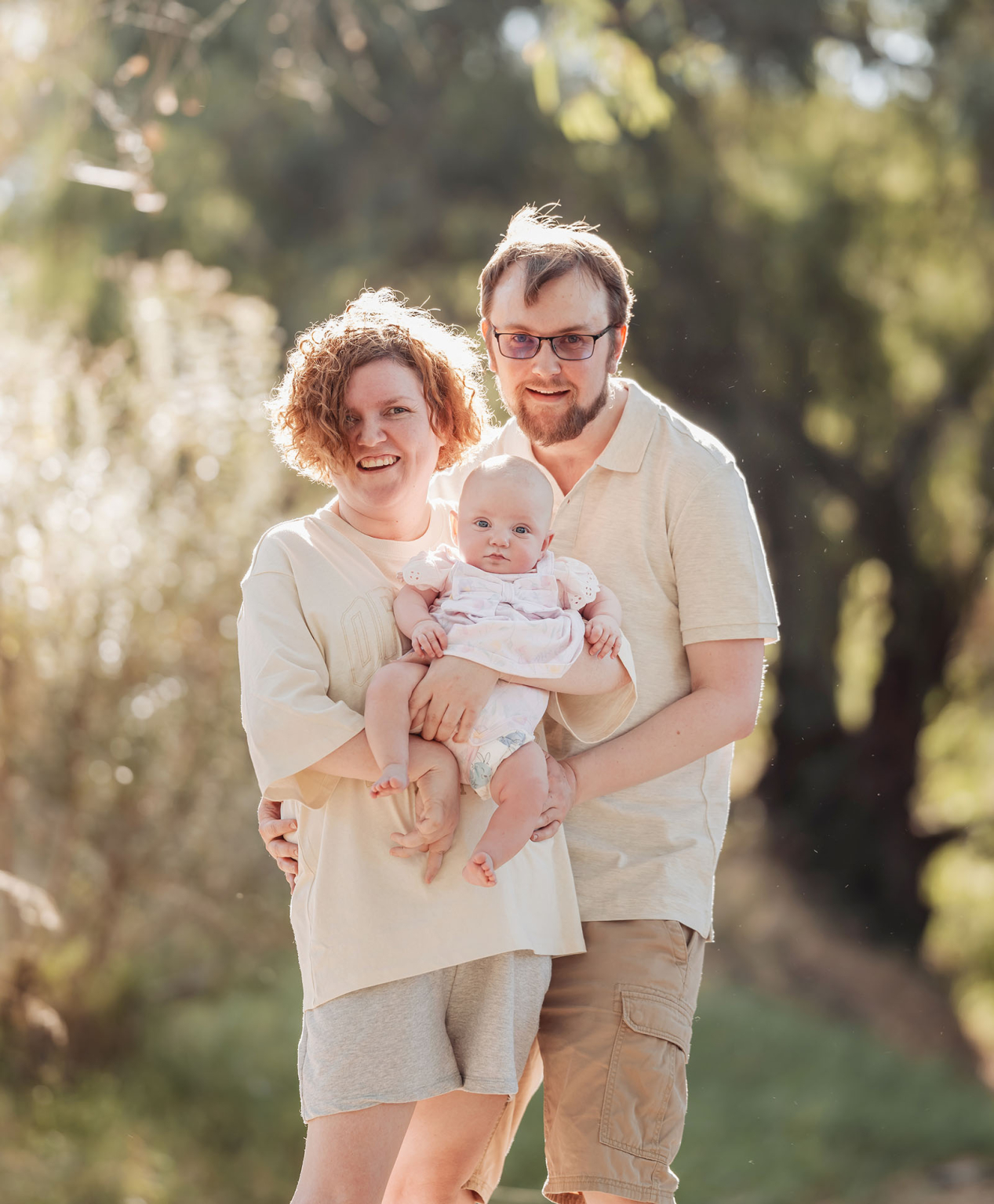 carisbrooke park family photoshoot 66 Happy family with baby enjoying a sunny day in a green park setting.