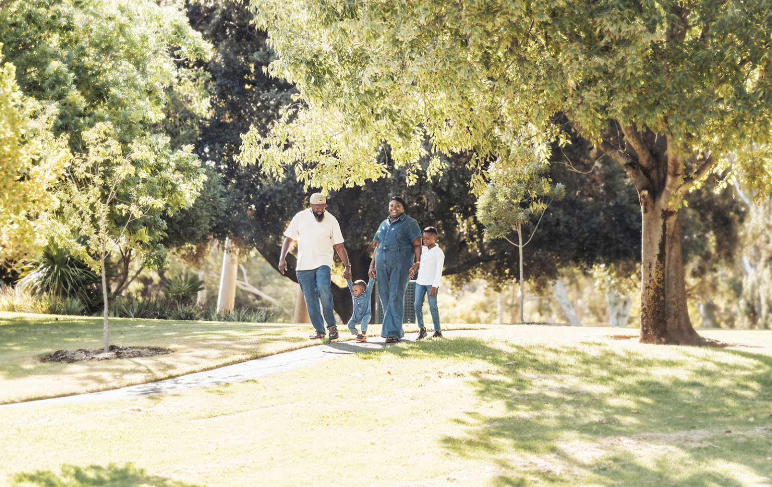 family photoshoot in veale gardens 16 Family strolling in sunlit park, enjoying nature and time together.