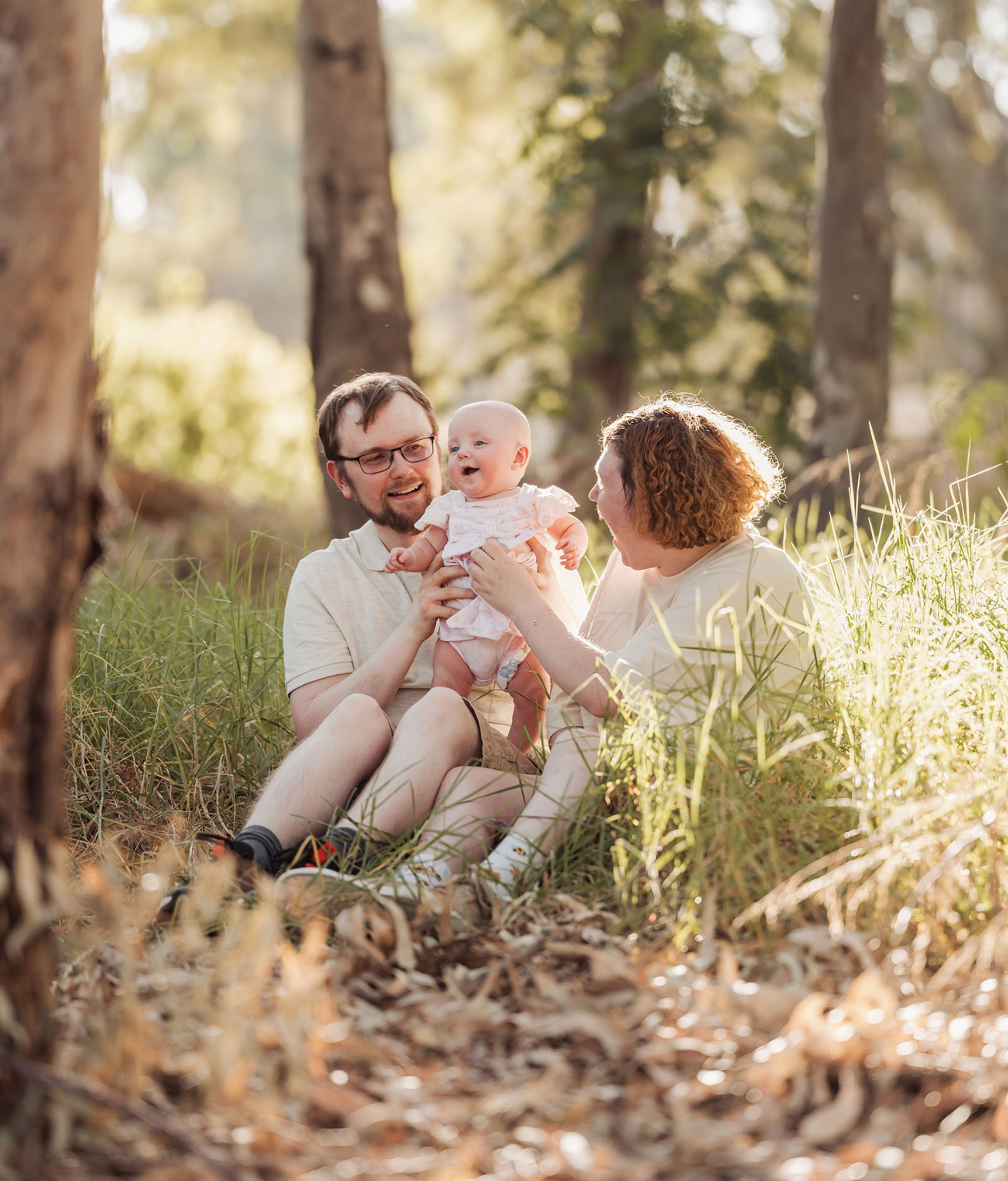 carisbrooke park family photoshoot 78 Woodland family moment with smiling parents and baby in a sunlit forest.