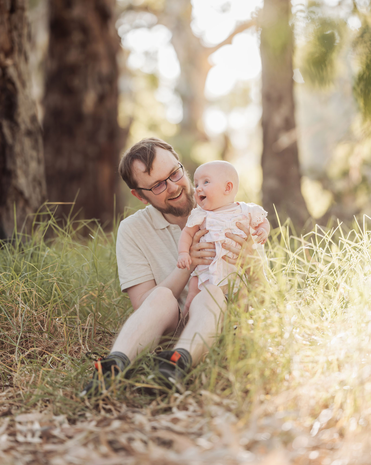 carisbrooke park family photoshoot 79 Father and baby enjoying a serene moment in lush, sunlit natural setting.