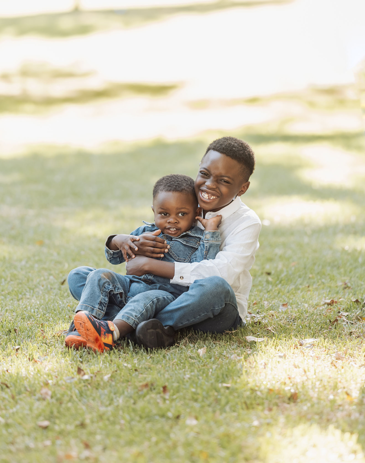 family photoshoot in veale gardens 13 Two joyful siblings embrace on a sunlit grassy field, showcasing sibling love and happiness.