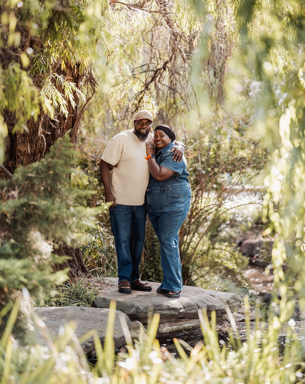 family photoshoot in veale gardens 6 Couple embracing under willow tree, surrounded by lush greenery, near a pond.