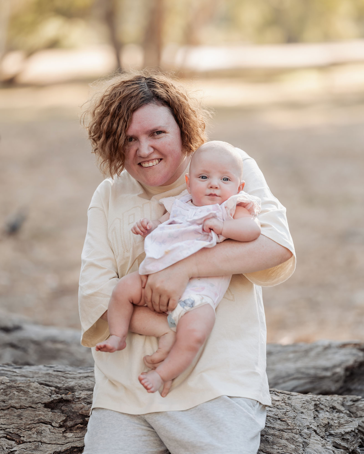 carisbrooke park family photoshoot 73 Smiling adult holding baby in park with trees and sunlight, capturing joyful outdoor moment.