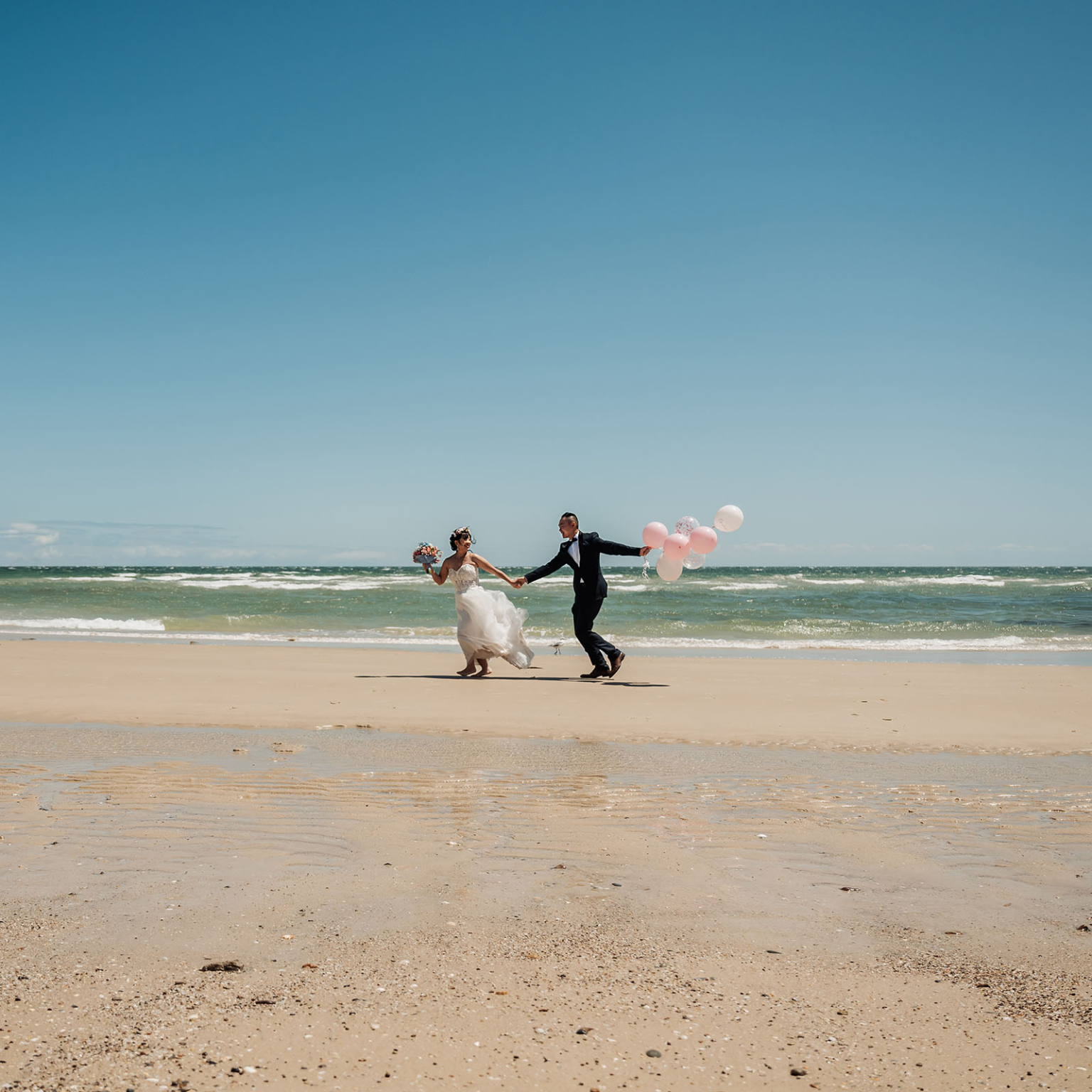 bumbunga lake photoshoot - tina & eric 29 Newlywed couple joyfully runs on beach with balloons, bride in white gown and flower crown.