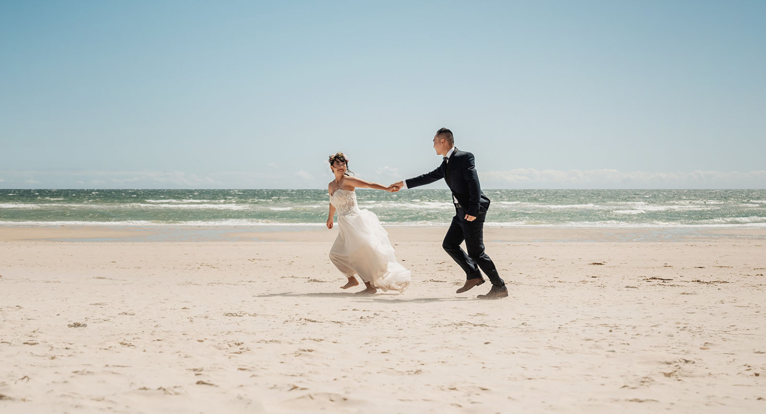 bumbunga lake photoshoot - tina & eric 45 Bride and groom joyfully running barefoot on a serene beach during their wedding.