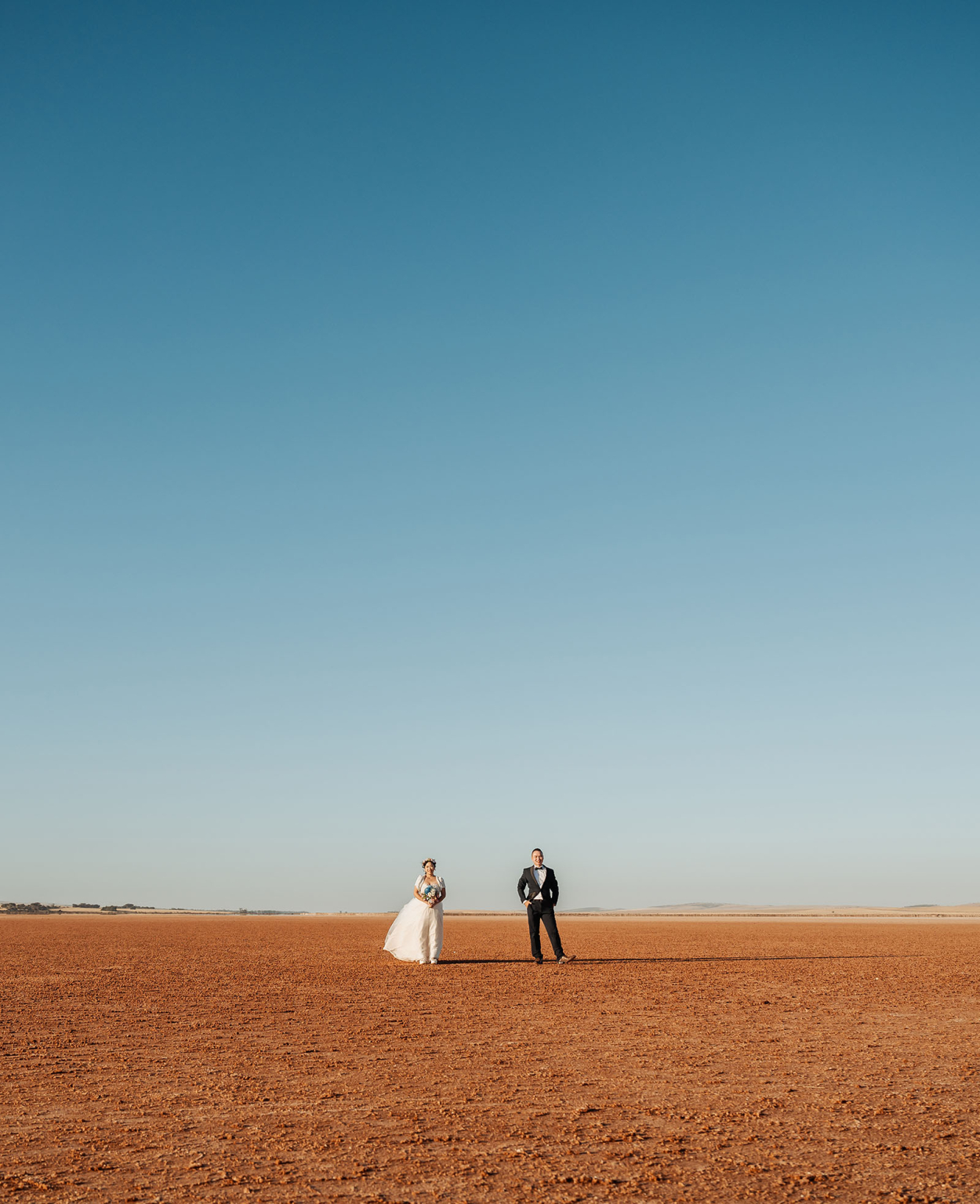 bumbunga lake photoshoot - tina & eric 80 Bride and groom in wedding attire on arid desert landscape under clear blue sky.