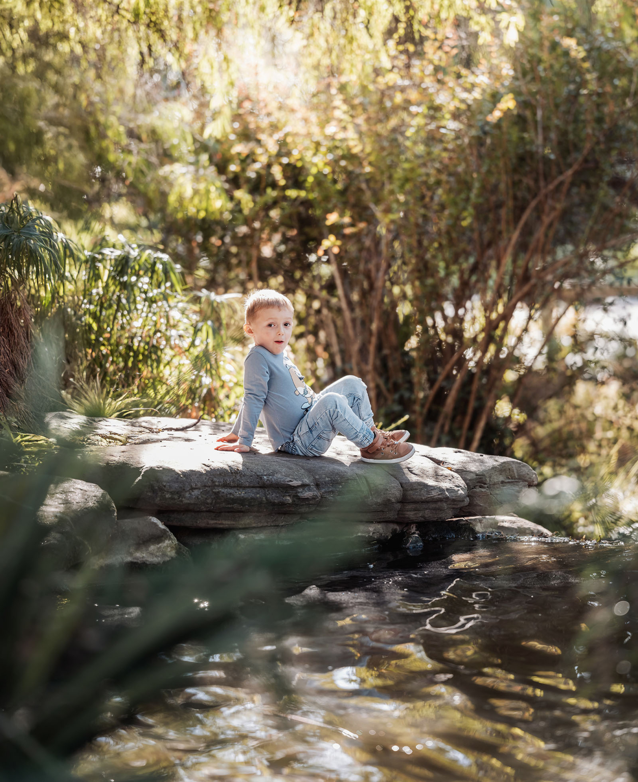 veale gardens family photography 102 Child in peaceful park setting, sitting on rock by pond, surrounded by lush greenery.