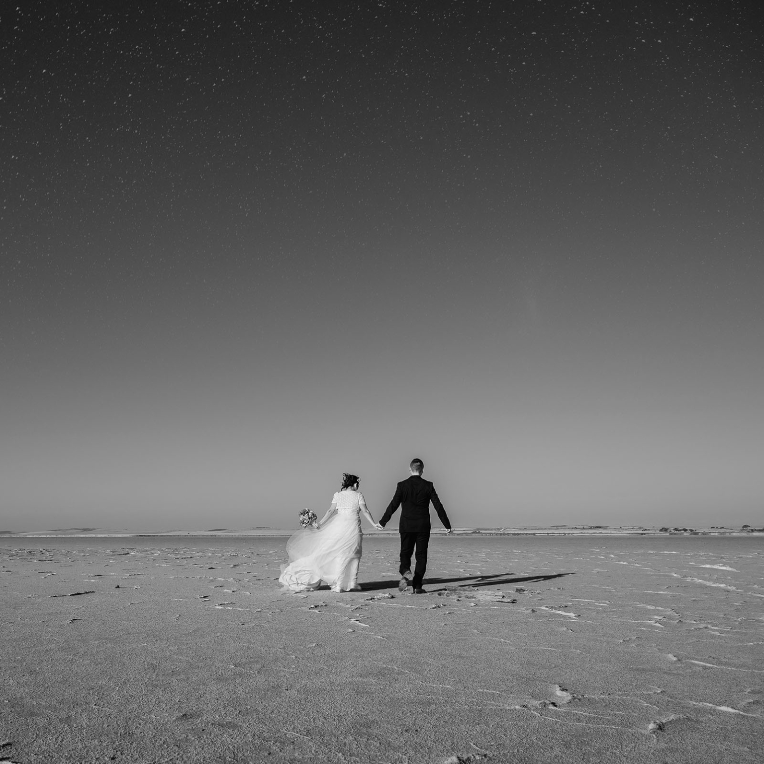 bumbunga lake photoshoot - tina & eric 69 Bride and groom on empty beach under starry sky, black and white photograph.