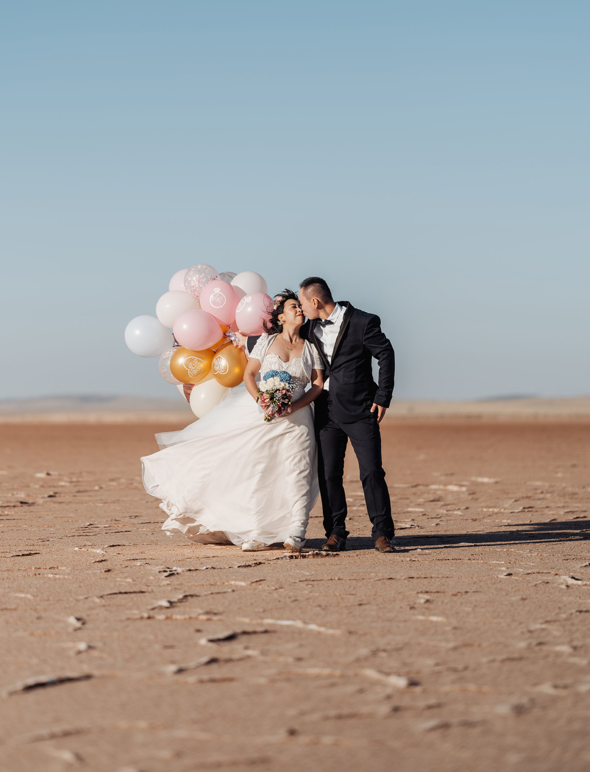 bumbunga lake photoshoot - tina & eric 67 Romantic desert wedding photo with couple kissing amid balloons and arid landscape.