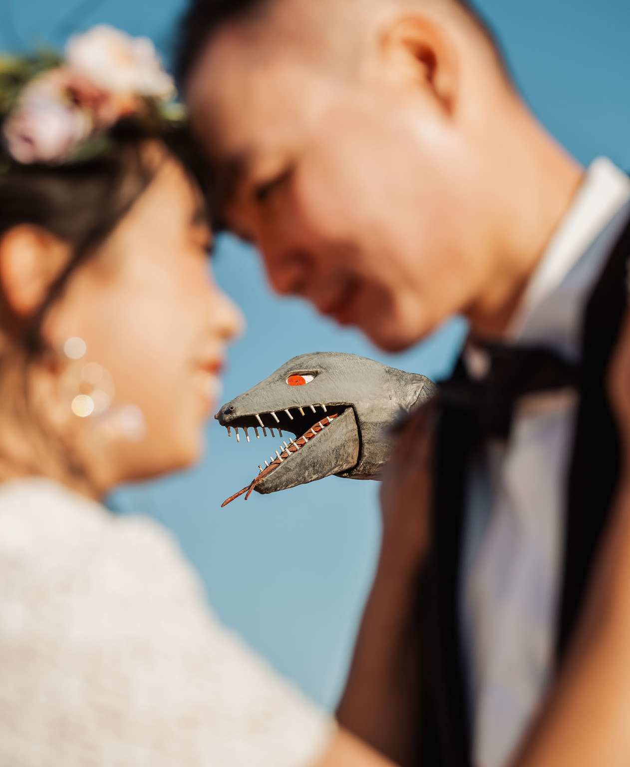 bumbunga lake photoshoot - tina & eric 78 Romantic couple with floral crown and playful dinosaur puppet under a clear blue sky.