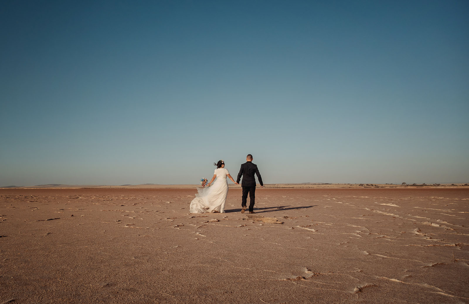 bumbunga lake photoshoot - tina & eric 70 Newlyweds walk hand-in-hand across a barren desert landscape, embracing adventure and new beginnings.