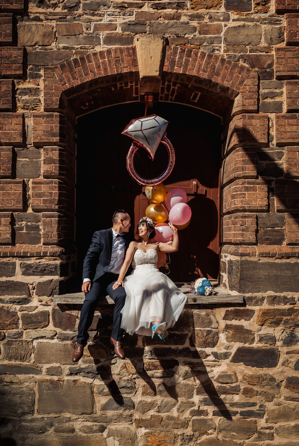 bumbunga lake photoshoot - tina & eric 56 Bride and groom on rustic ledge, balloons, stone wall, archway, romantic wedding scene.