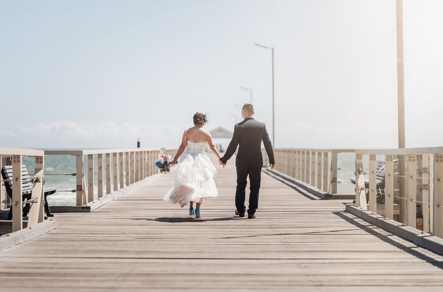 bumbunga lake photoshoot - tina & eric 42 Bride and groom walking hand-in-hand on a pier by the sea, symbolizing love and unity.