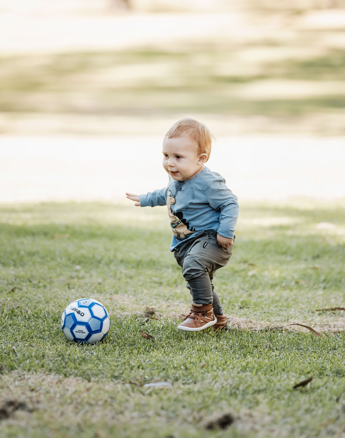 veale gardens family photography 117 Toddler playing on grass with soccer ball, showcasing determination and curiosity in natural daylight.