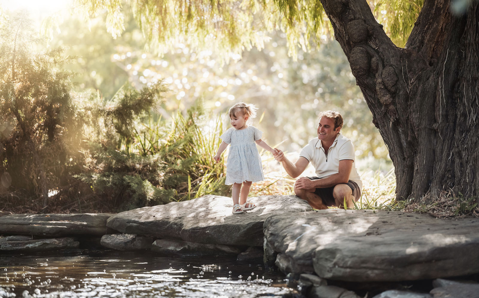 veale gardens family photoshoot 3 Child and father bonding by a serene stream in a lush natural setting.