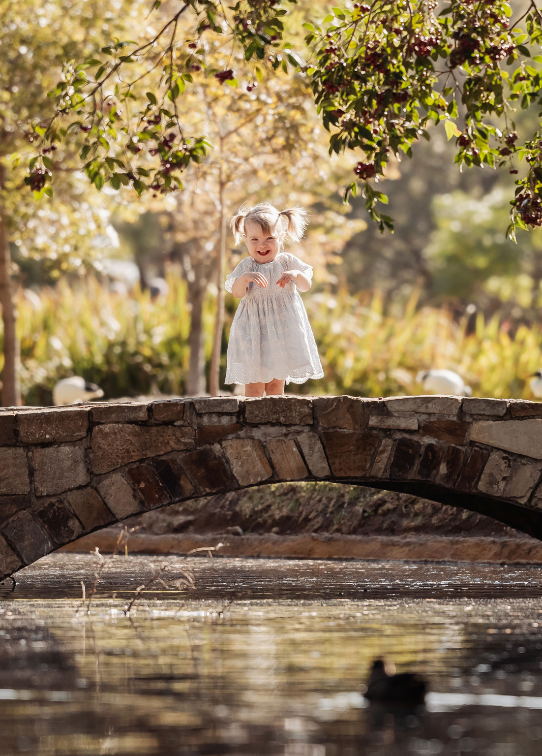 veale gardens family photoshoot 10 Girl in white dress smiles on stone bridge surrounded by vibrant nature.