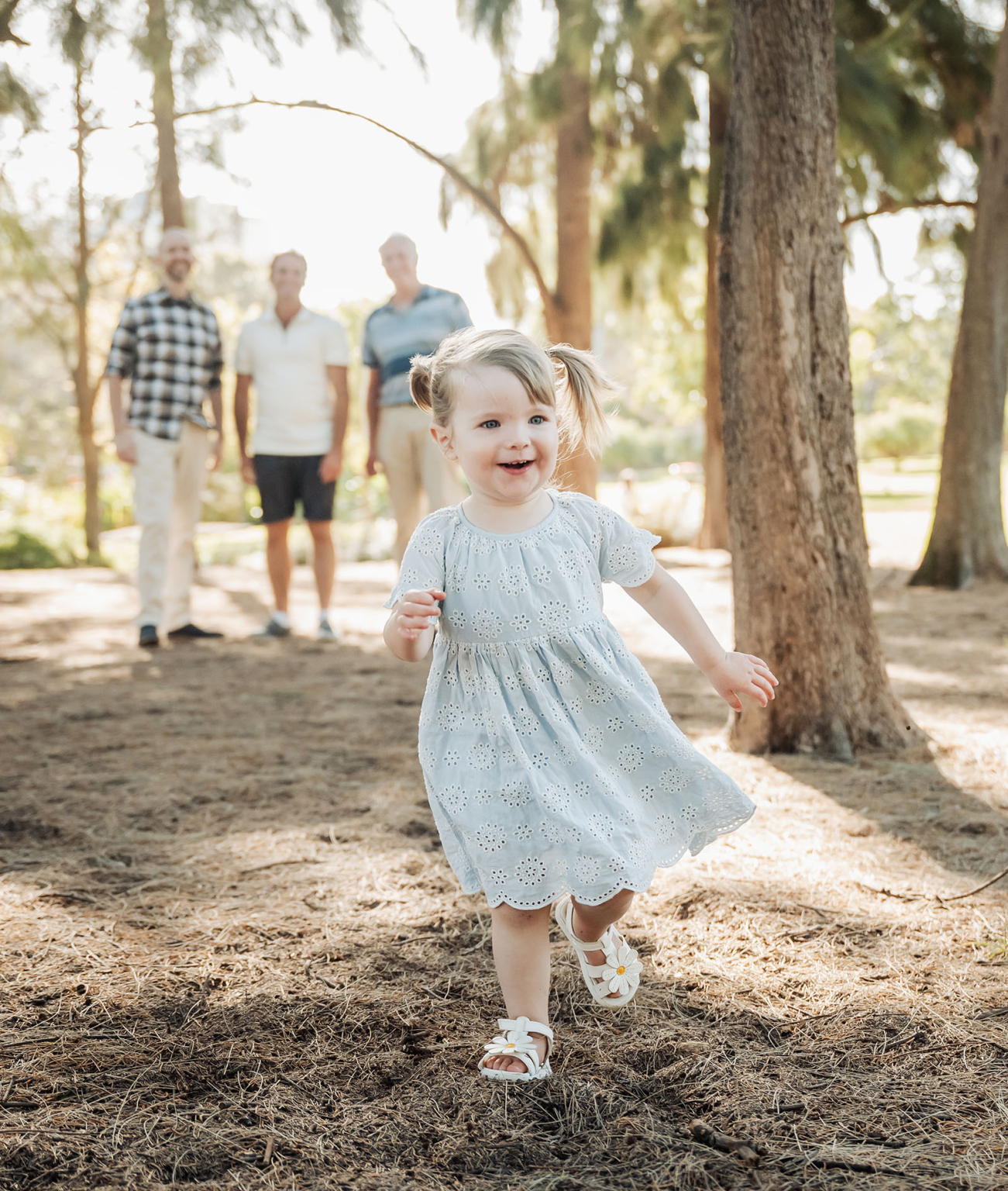 veale gardens family photoshoot 16 Young girl joyfully running in a sunlit park, wearing a light blue dress.