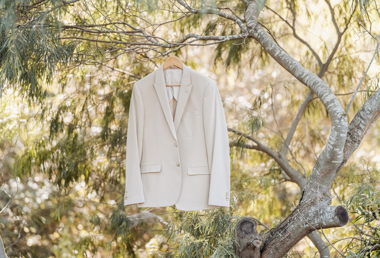 wedding at kuitpo hall - sophia & sam 81 Beige suit jacket on tree, blending elegance with nature; serene outdoor setting.