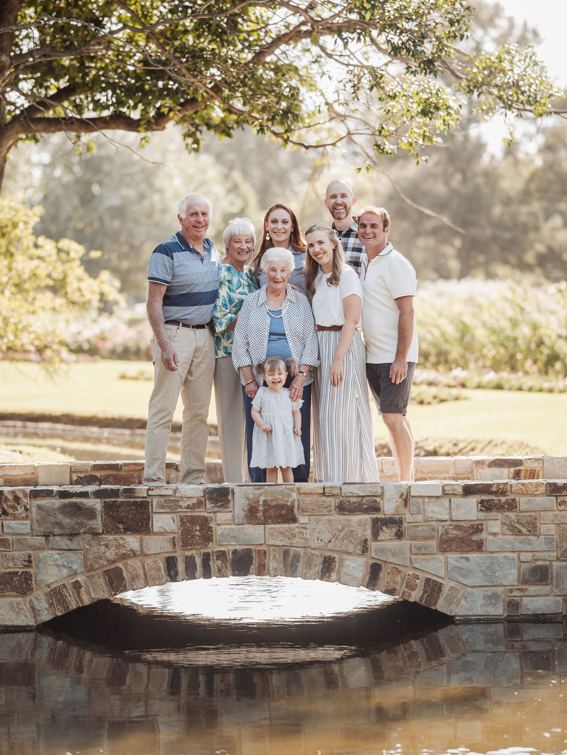 veale gardens family photoshoot 9 Multigenerational family on stone bridge in sunny park, celebrating unity and natures harmony.