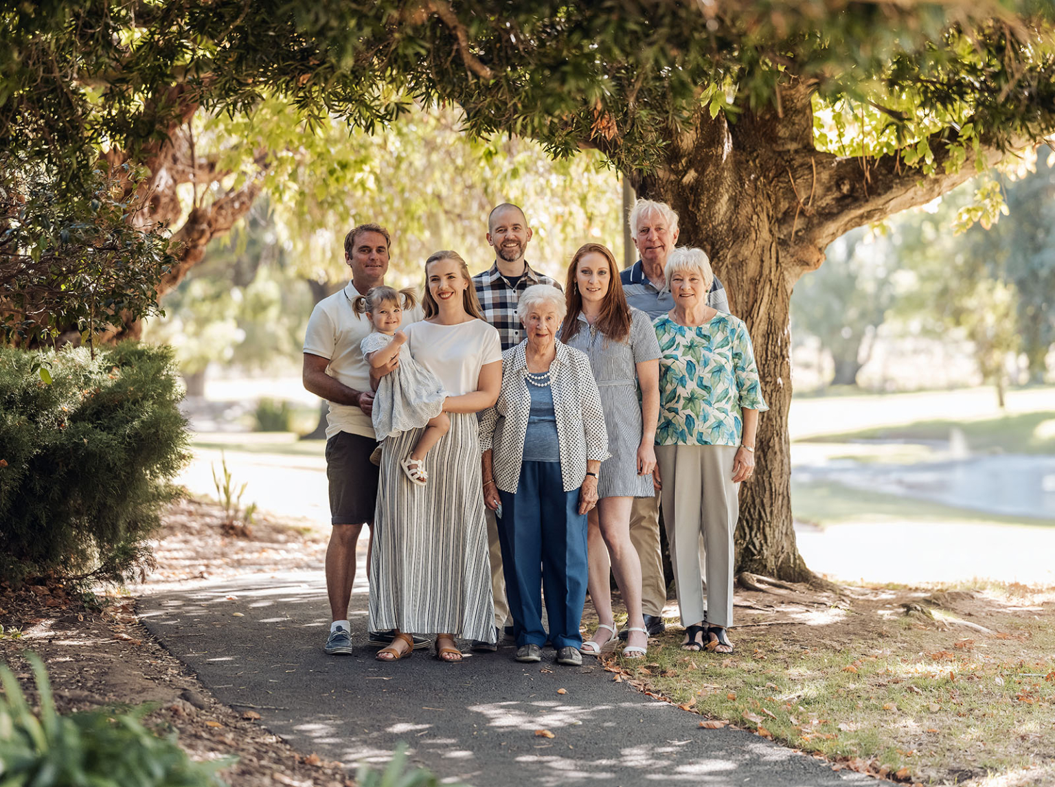 veale gardens family photoshoot 4 Multigenerational family posing outdoors in a park, surrounded by greenery and sunlight.