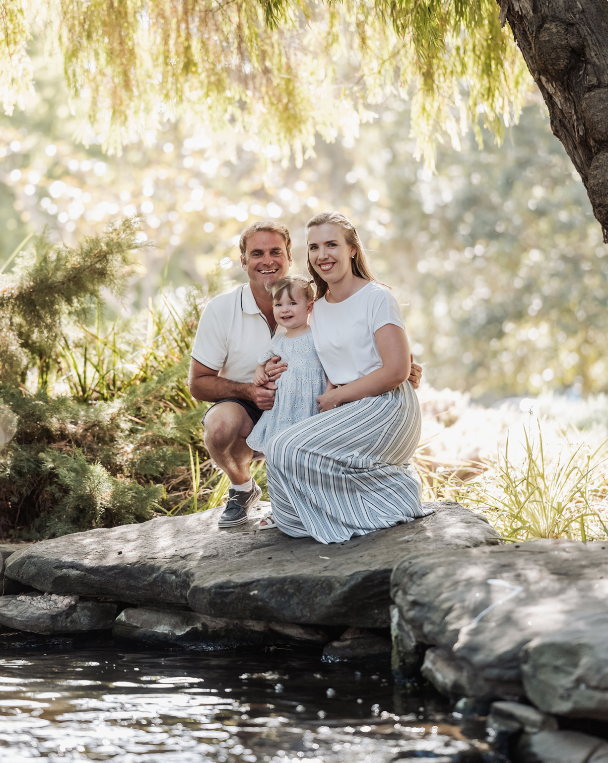 veale gardens family photoshoot 1 Family enjoying nature by stream, under tree, sharing joy, serenity, and togetherness.