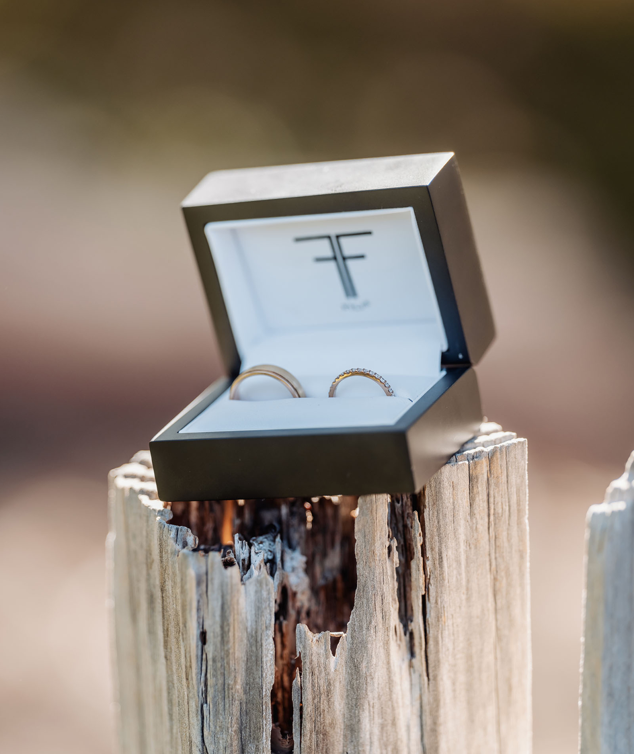 wedding at kuitpo hall - sophia & sam 82 Elegant wedding and engagement rings in luxury box on rustic wooden post backdrop.