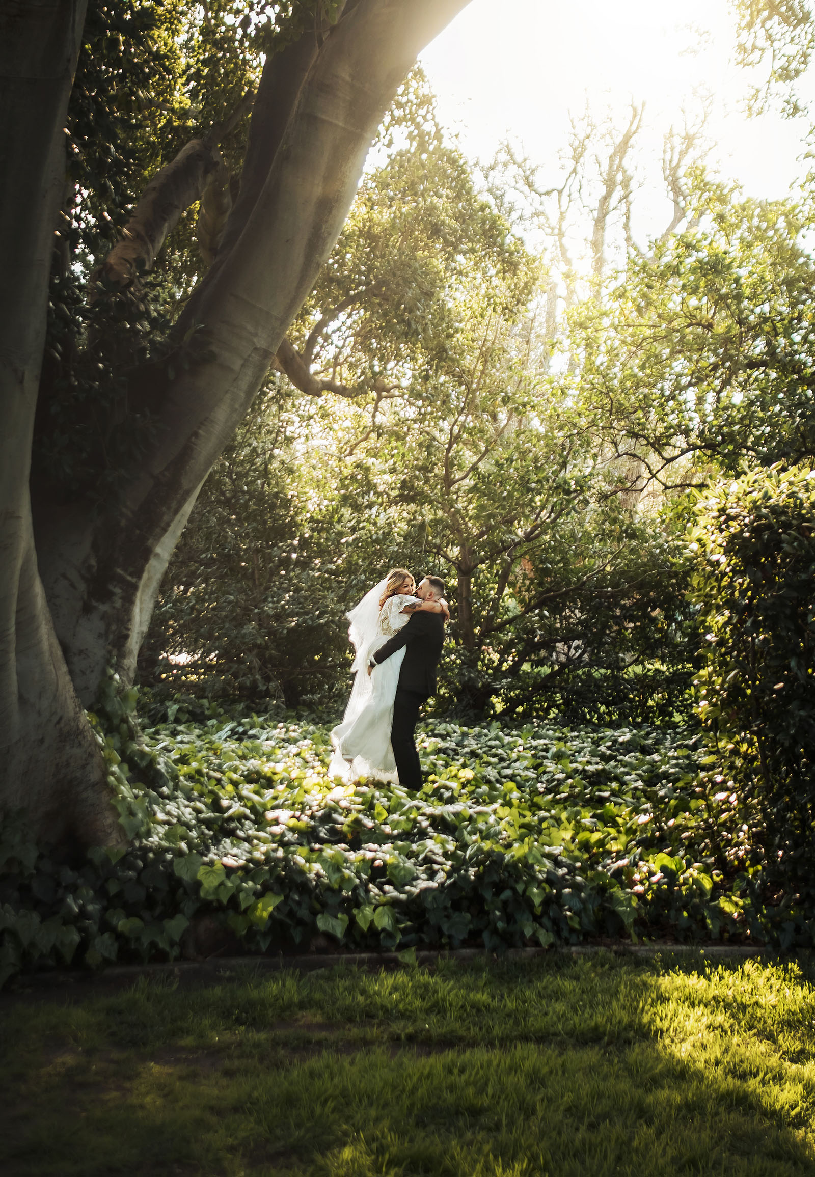 botanic gardens adelaide wedding - melanie & adrian 247 Bride and groom embrace in a lush forest setting during a woodland wedding ceremony.