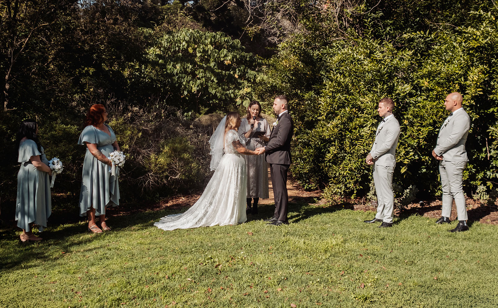 botanic gardens adelaide wedding - melanie & adrian 227 Elegant outdoor wedding ceremony under sunny skies with floral decorations.
