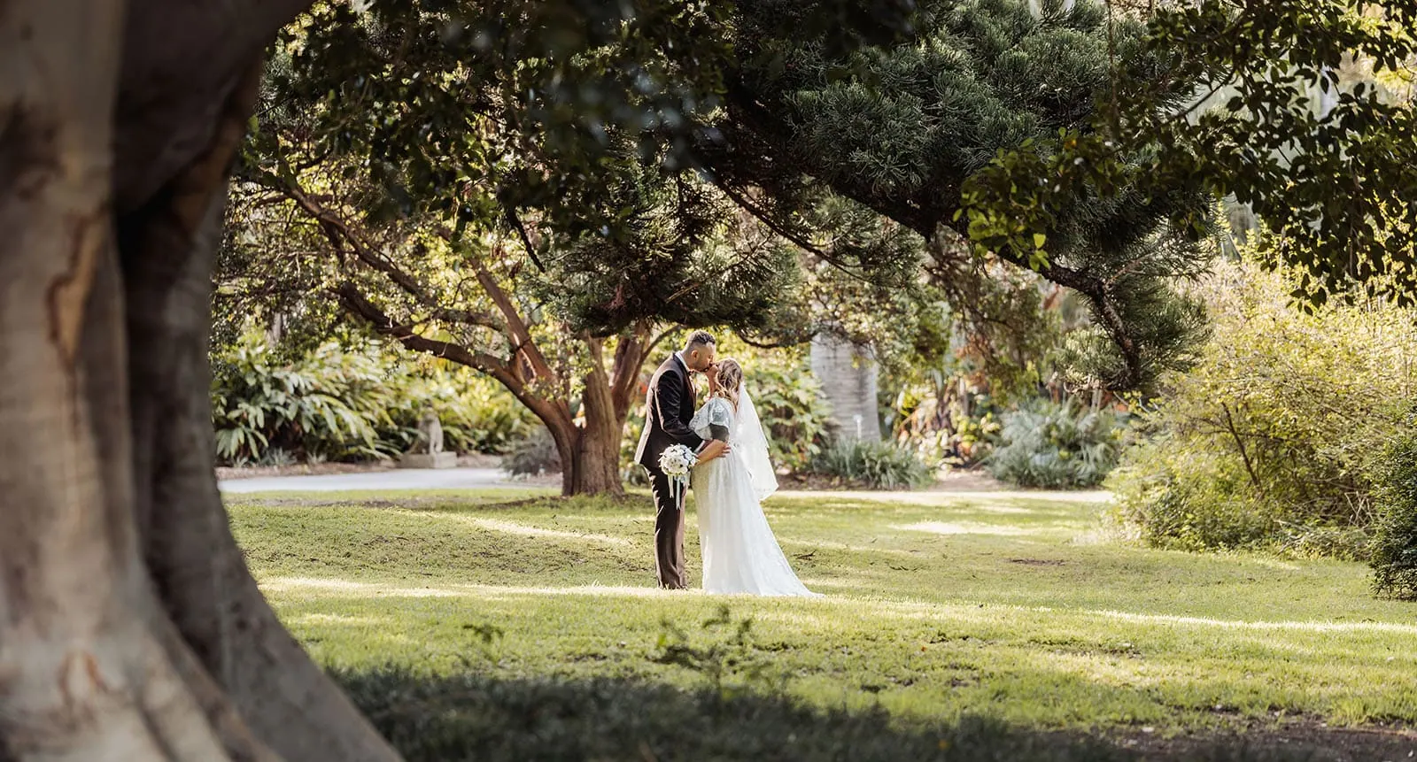 botanic gardens adelaide wedding - melanie & adrian 242 Bride and groom embrace in a lush garden setting during their wedding ceremony.