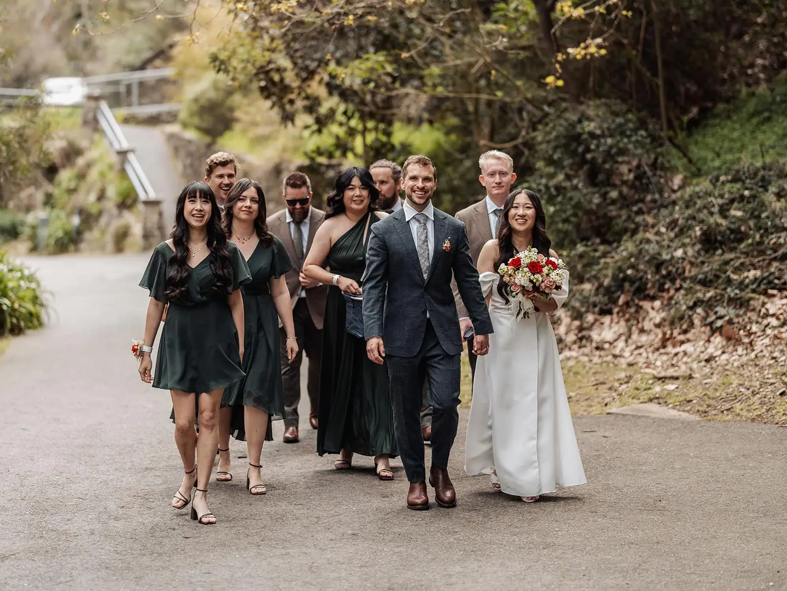 utopia waterfall gully wedding - sally & ben 240 Bride and groom walking in wedding procession with flowers and guests in elegant attire.