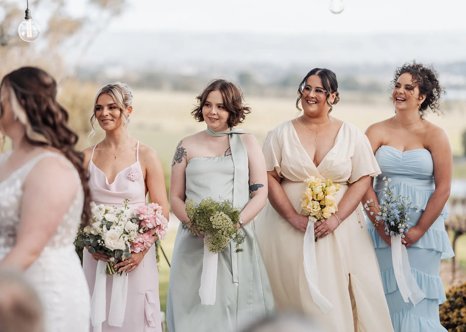 beach rd wines wedding - hana & jessie 58 Bridesmaids in pastel dresses celebrate a vibrant outdoor wedding ceremony.