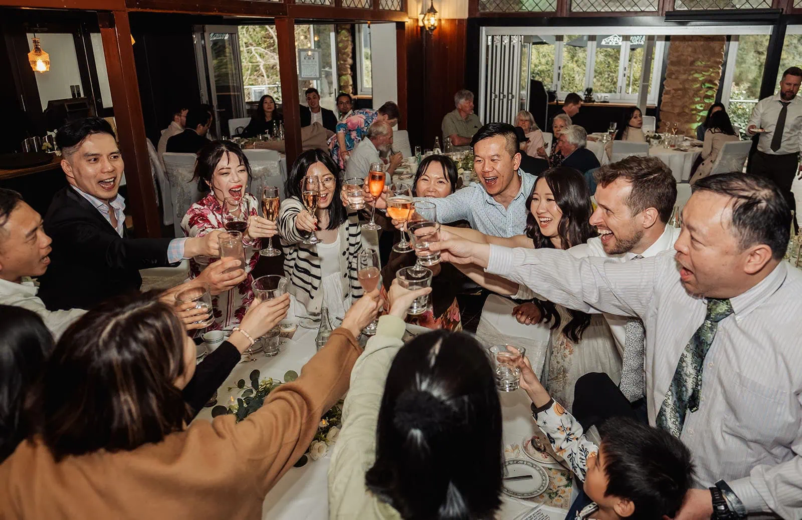 utopia waterfall gully wedding - sally & ben 259 Group raising glasses in festive celebration, sharing joy and laughter.