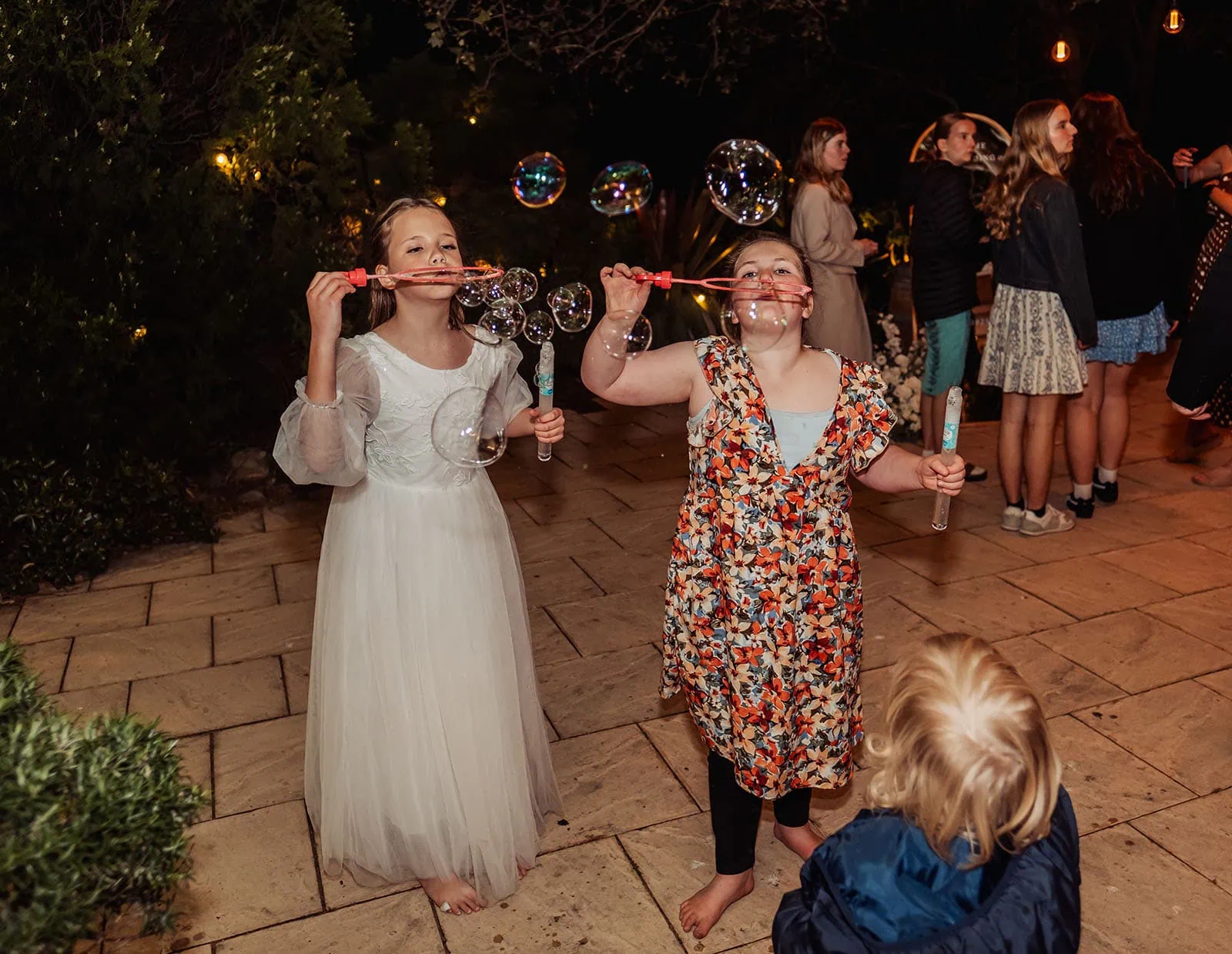beach rd wines wedding - hana & jessie 94 Children playing outside, happily blowing soap bubbles at a park event.