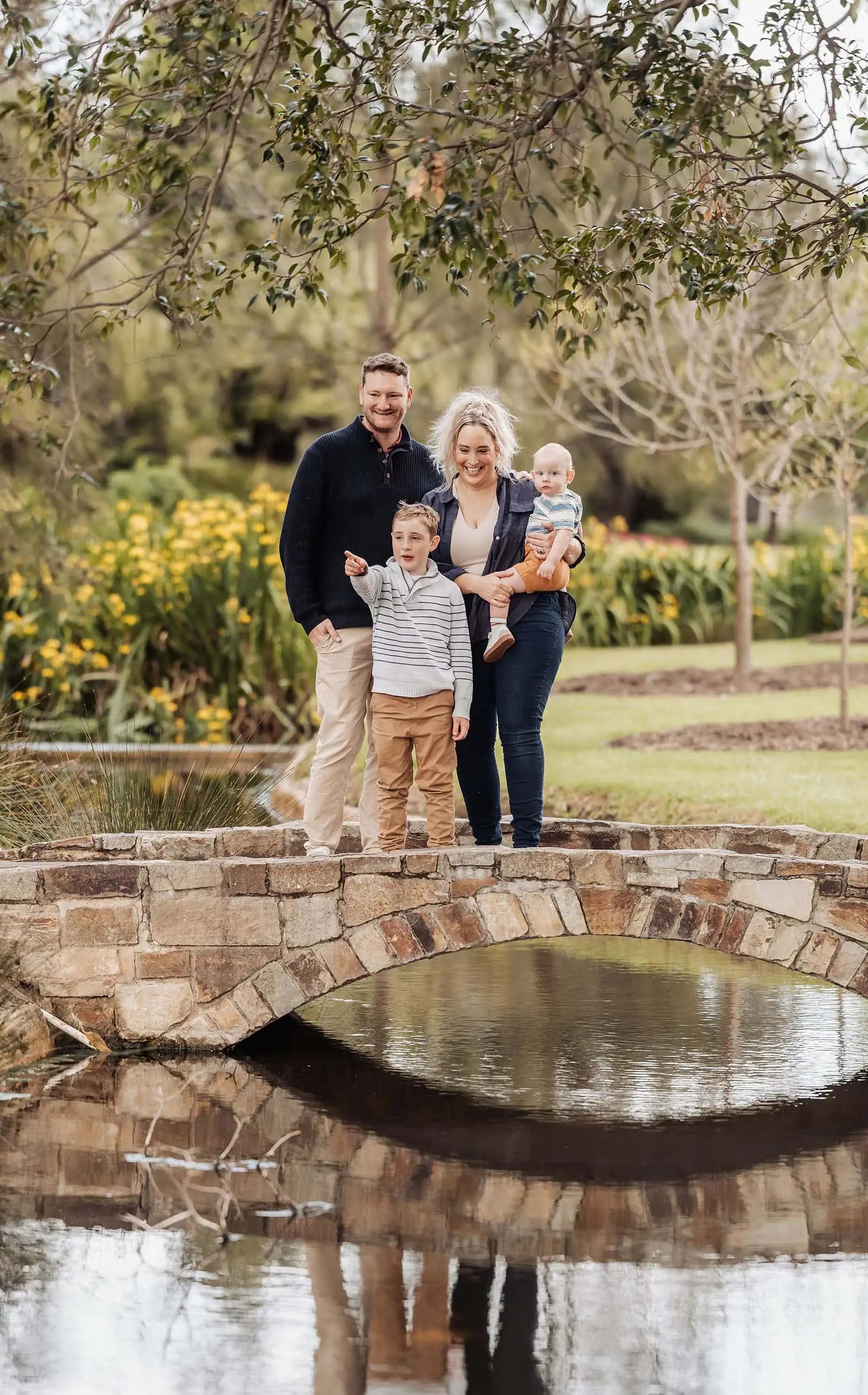 southern parklands family photography 32 Family smiling on a scenic bridge during a sunny day.