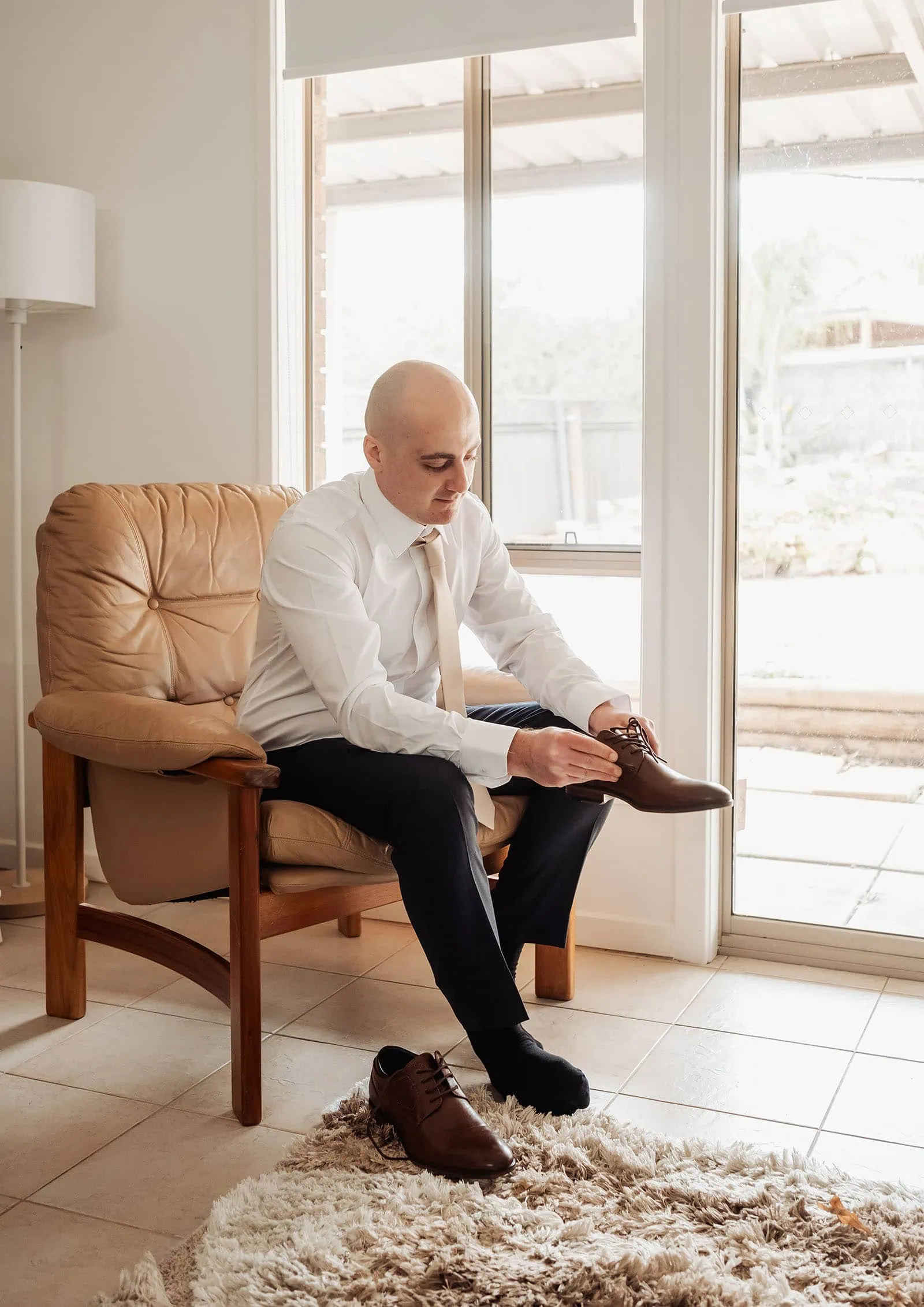 grand cru estate wedding - isabella & nick 98 Man tying shoelaces on leather shoes in a modern living room.