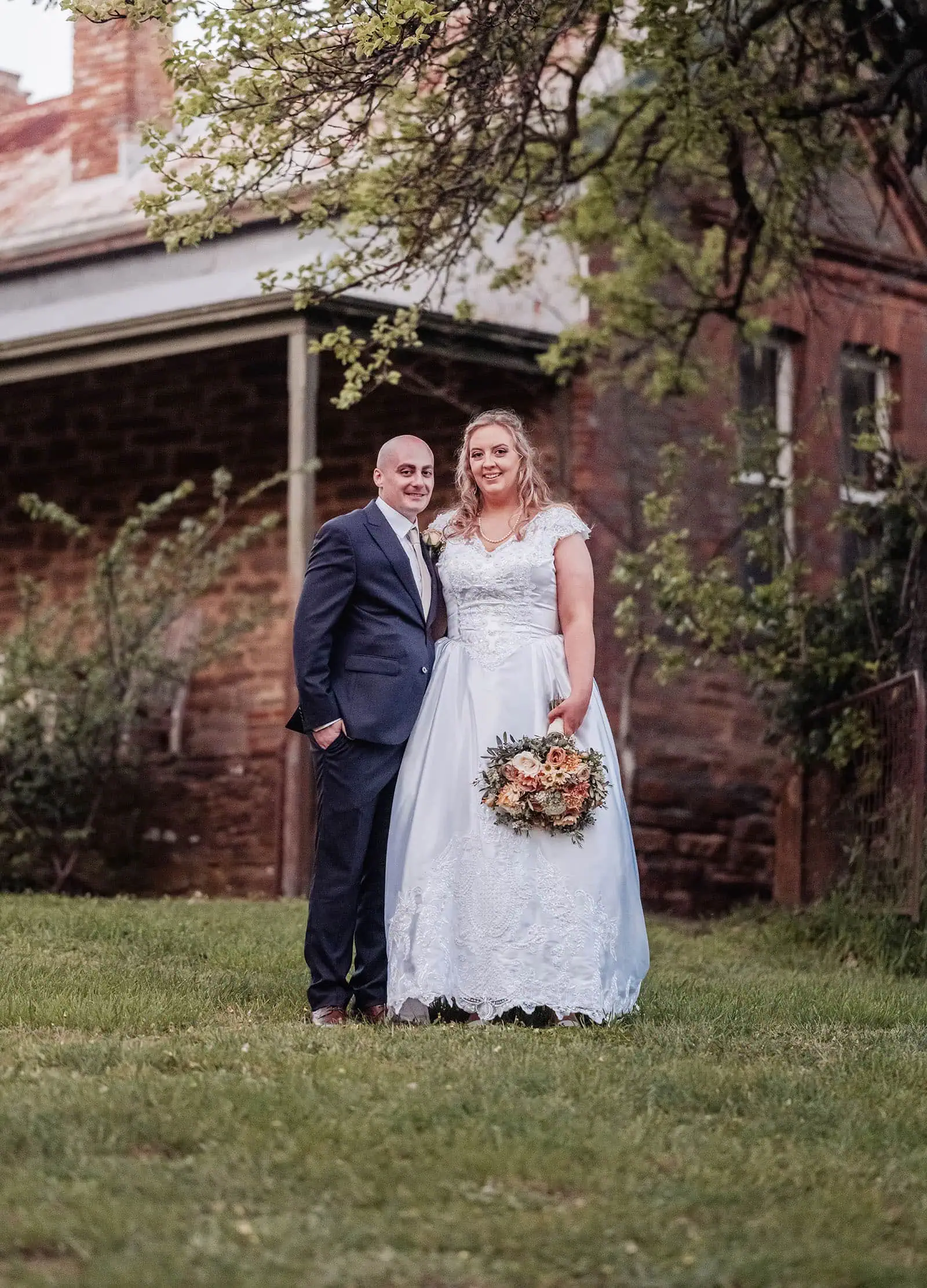 grand cru estate wedding - isabella & nick 151 Newlywed couple embracing by quaint rustic building in scenic outdoor setting.