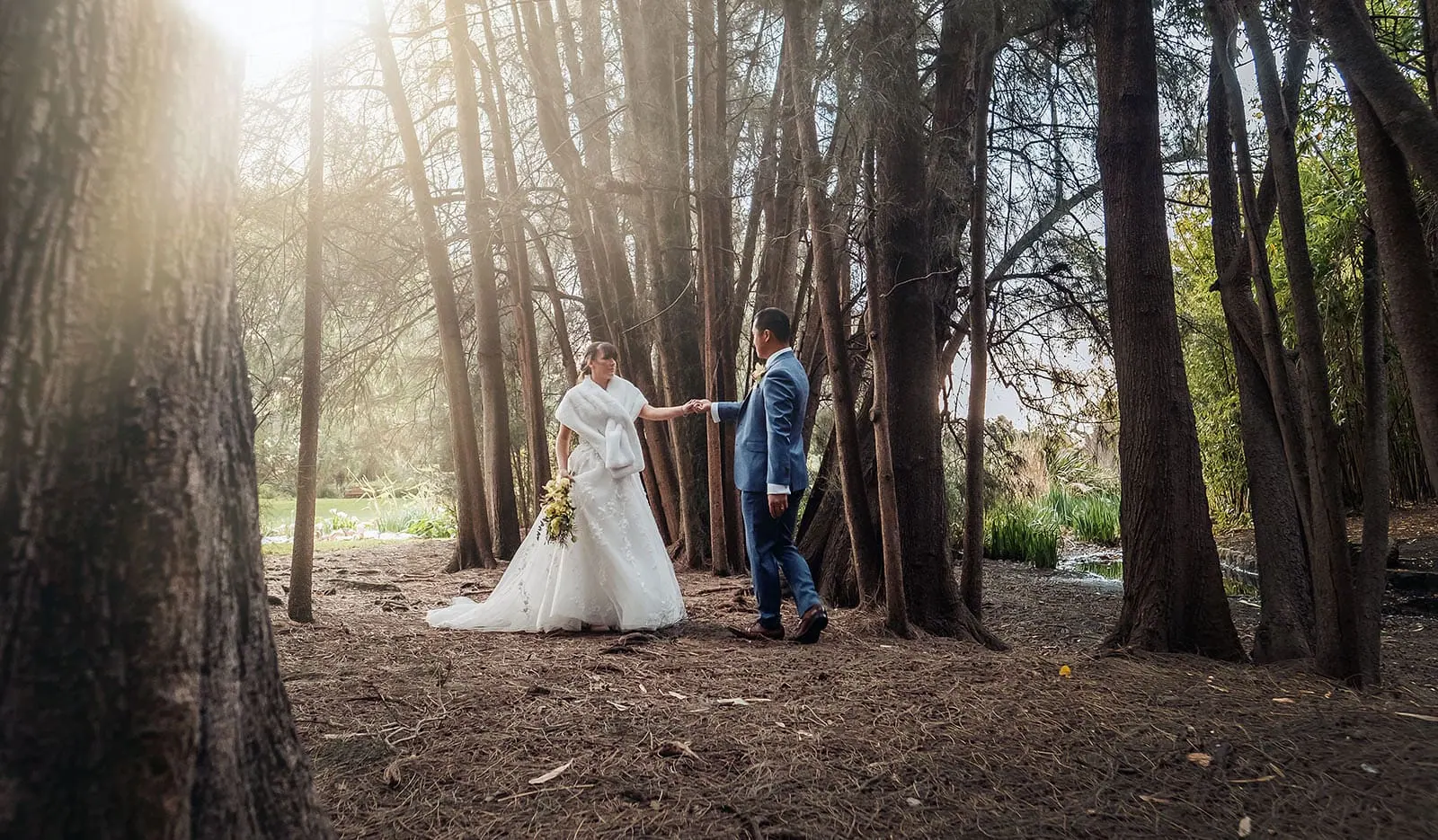 adelaide botanic gardens summerhouse wedding - belinda & ian 183 Newlyweds embracing in a lush forest setting, surrounded by green trees and romantic ambiance.